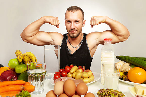 Вкаченный спортсмен на фоне фруктов и овощей